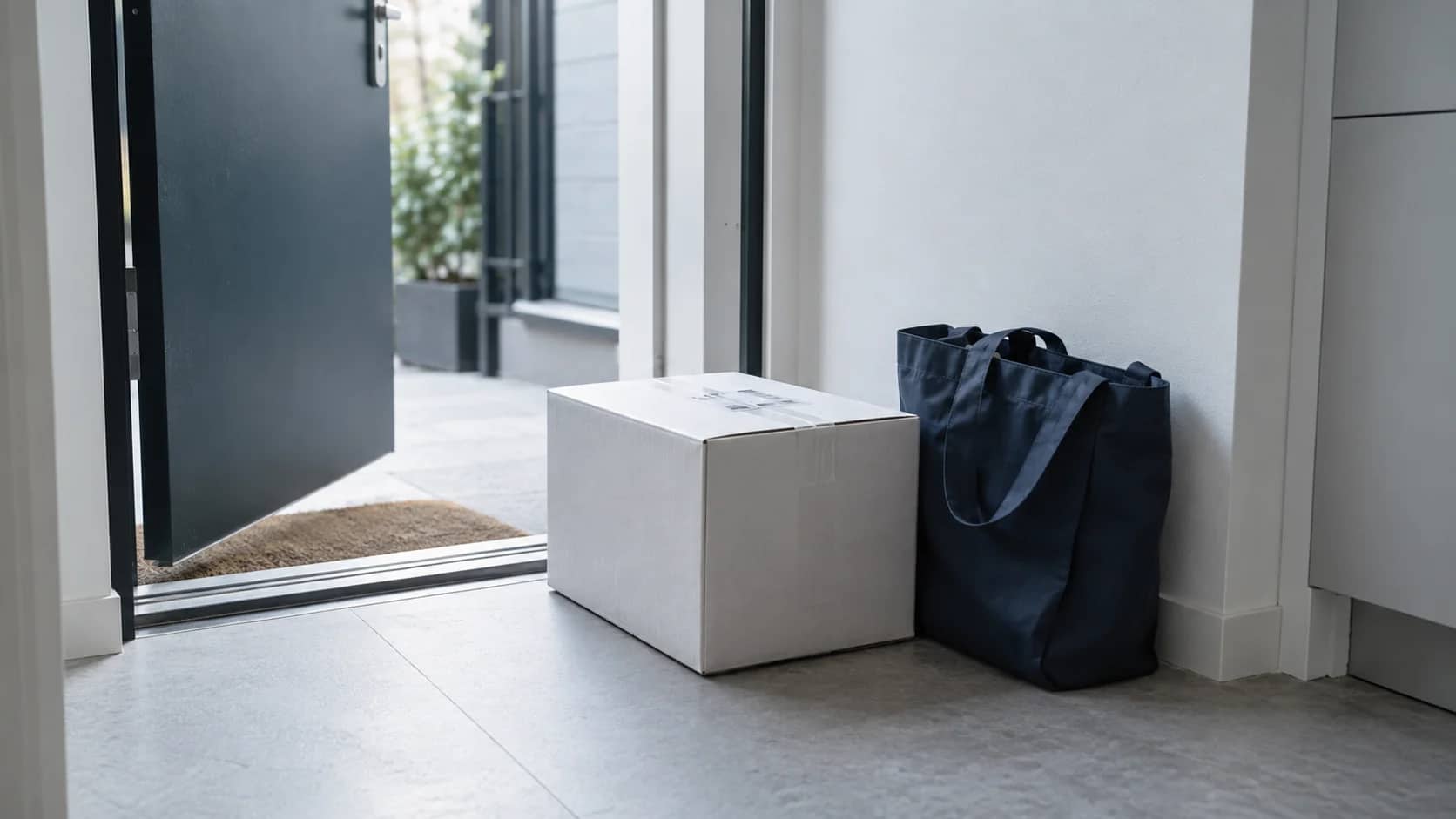 A delivered parcel and a reusable shopping tote beside an apartment doorway.